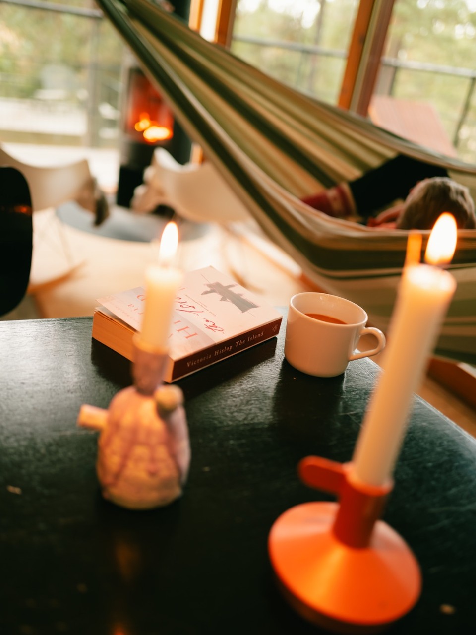 Lit candles, a book and a cup of tea on a dark table