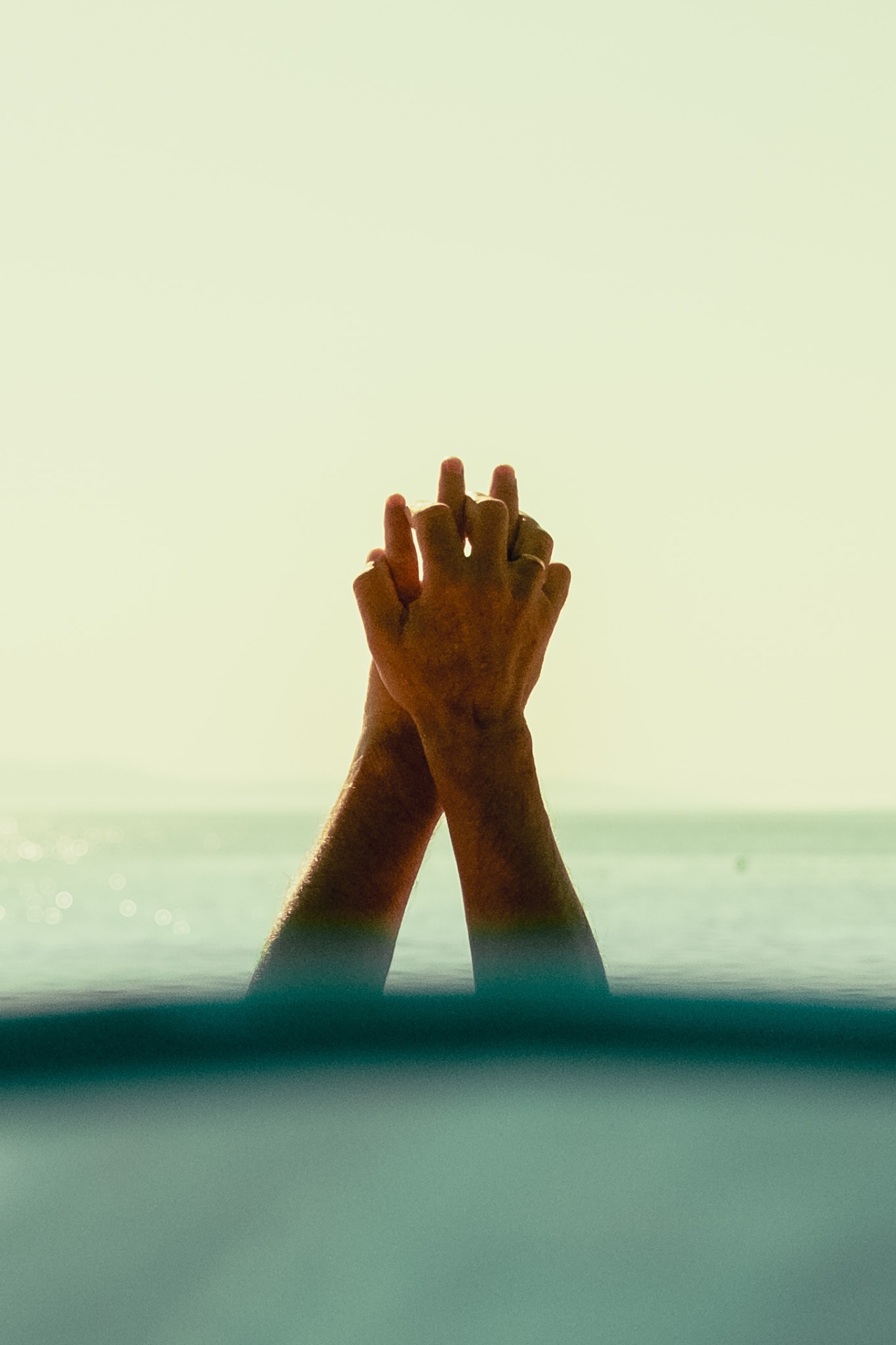 Clasped hands raised above the sea at dusk